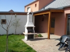 Zahradní krb Sázava s bílou fasádou. Krb má prodloužený komín o jeden nástave.